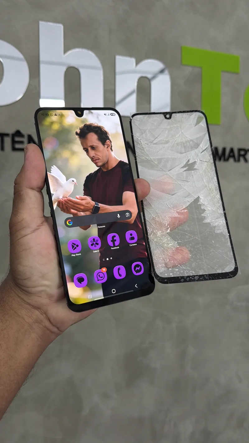 Cliente segurando celular com tela original ao lado do vidro trincado substituído na JohnTec